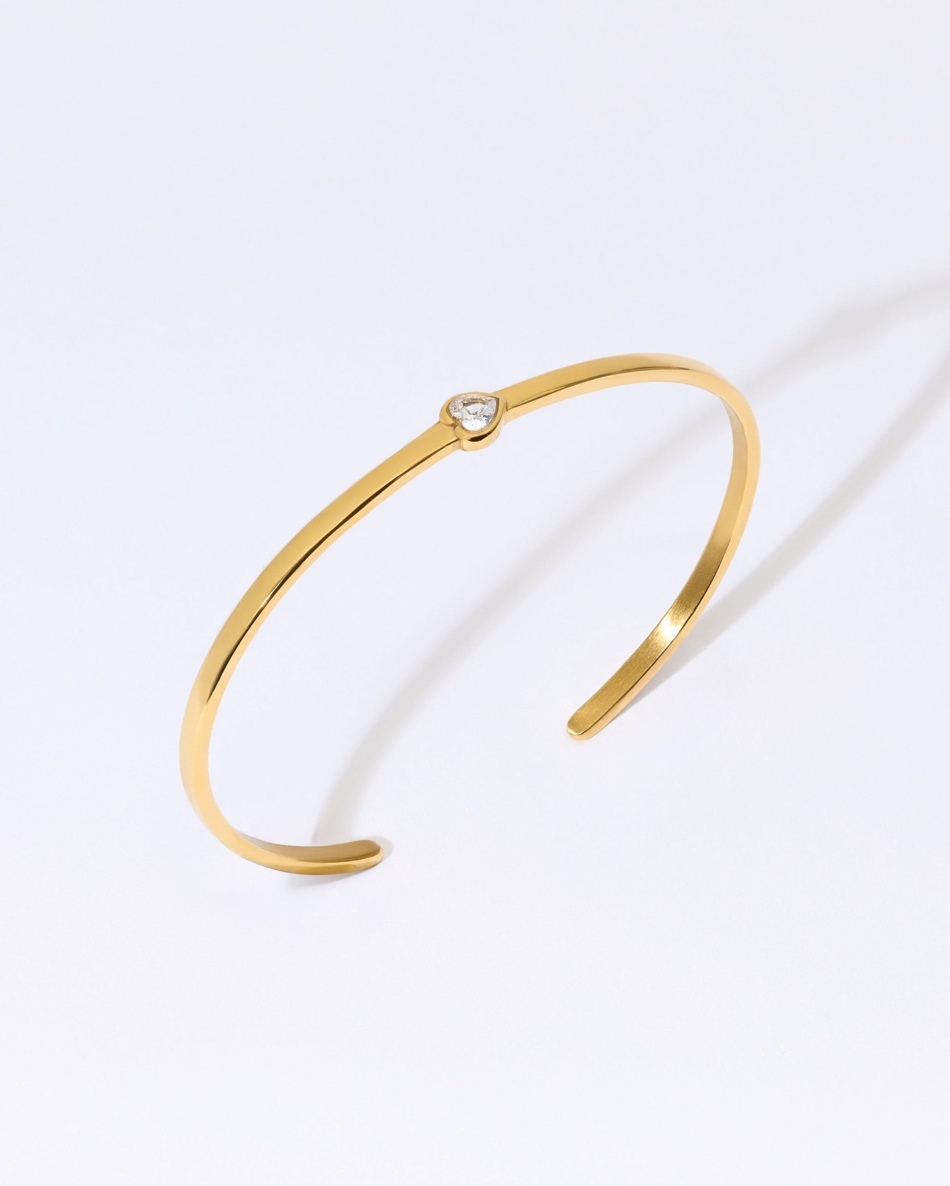 Gold bangle bracelet with heart gem on a white background