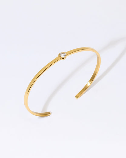Gold bangle bracelet with heart gem on a white background
