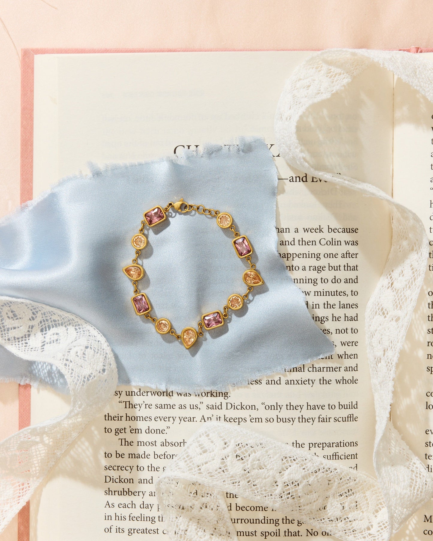 Meg Bracelet laying on an open book with blue cloth and lace.