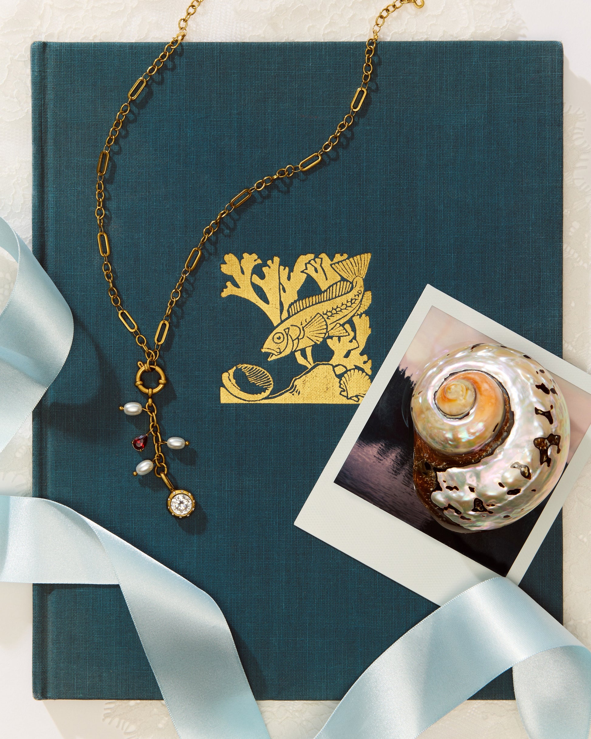The Poppy Necklace on a blue book with a polaroid photo of a shell.
