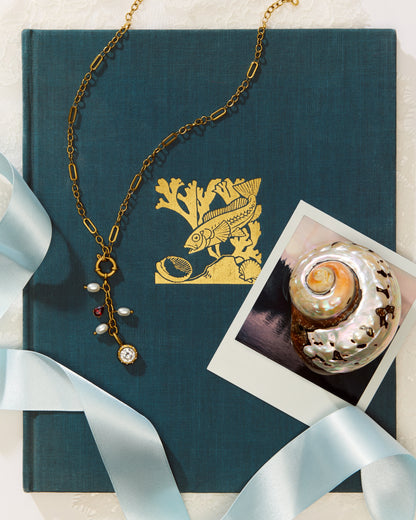 The Poppy Necklace on a blue book with a polaroid photo of a shell.