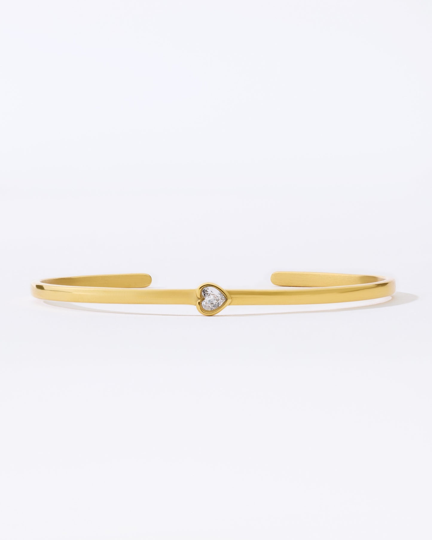 Gold bangle bracelet with a small heart shaped gemstone on a white background