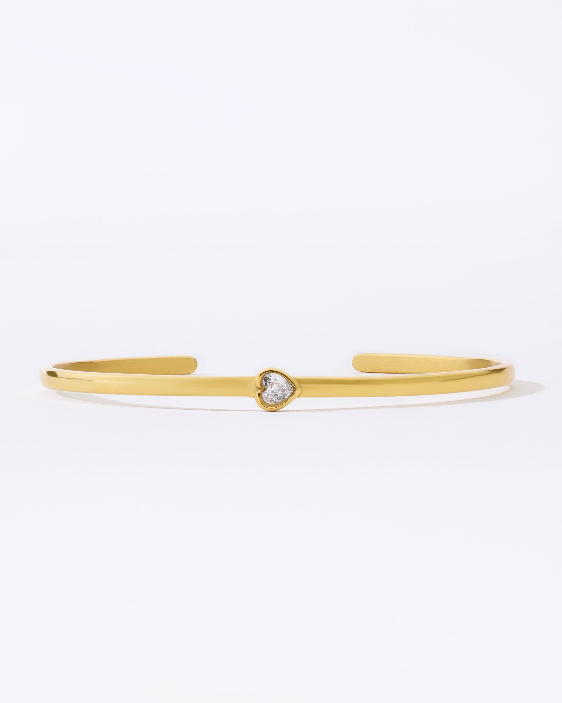 Gold bangle bracelet with a small heart shaped gemstone on a white background