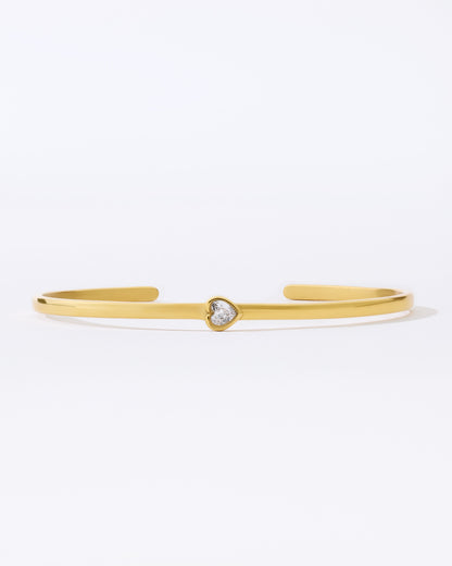 Gold bangle bracelet with a small heart shaped gemstone on a white background
